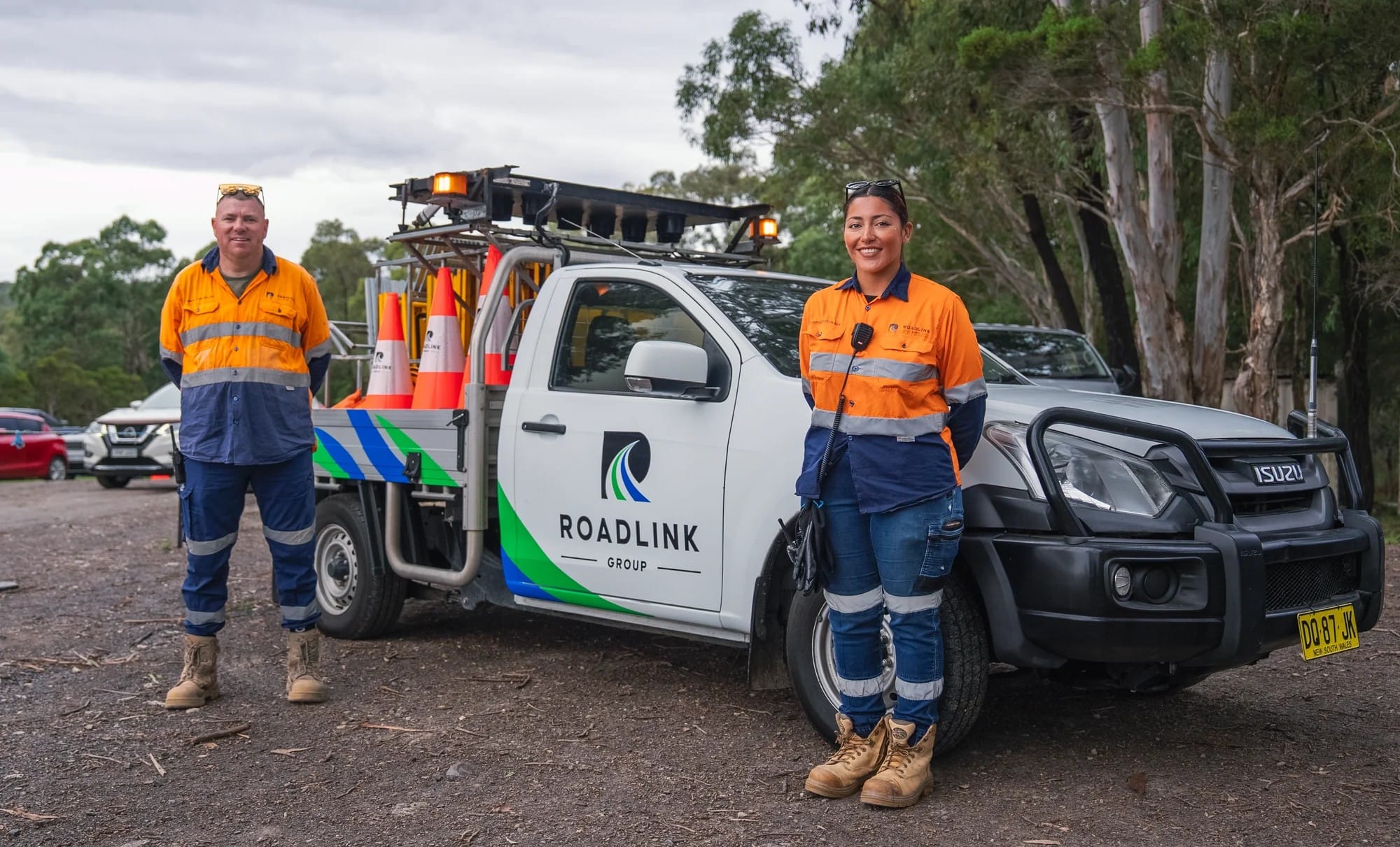 Two Roadlink Group traffic controllers standing with a branded traffic-control vehicle and equipment